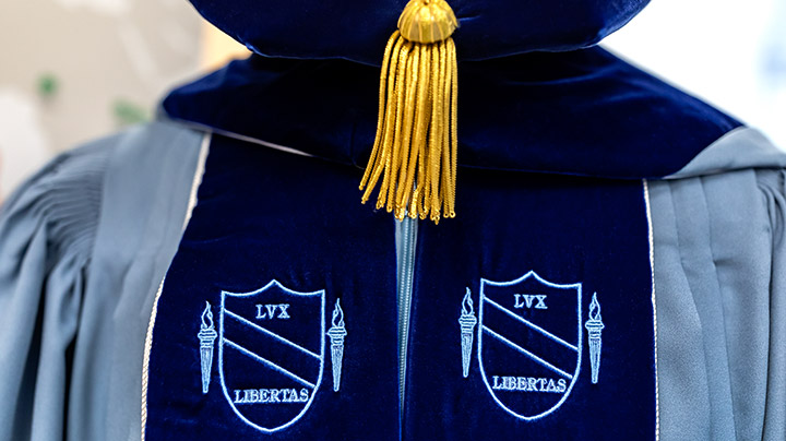 A close up of Carolina Blue doctoral regalia. There are two crests with the words 'Lux Libertas'