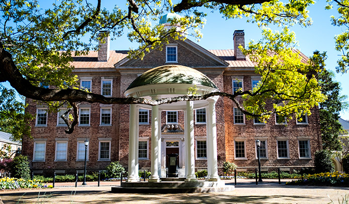 The Old Well with white columns in front of a brick building with tree brnaches in the foreground