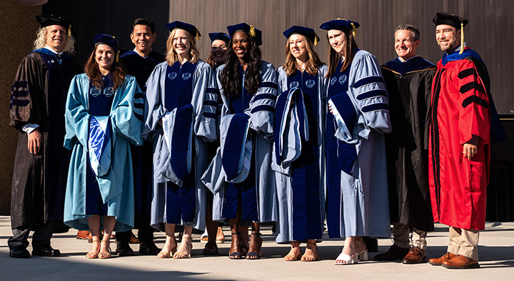 A group of graduate students and their advisors pose for photos outside of the Doctoral Hooding Ceremony