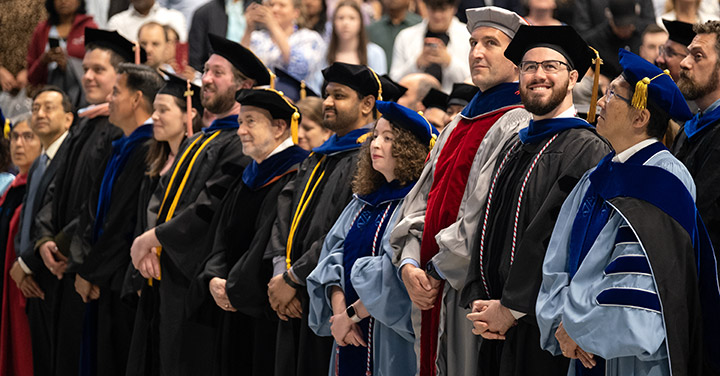 A row of graduate students and their advisors wearing colorful academic regalia at the Doctoral Hooding Ceremony