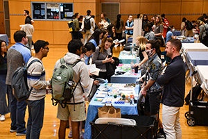 A view of a resource fair with numerous tables with staff and representatives interacting with students.