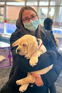 A student holds a golden retriever puppy who is sleeping in her arms.